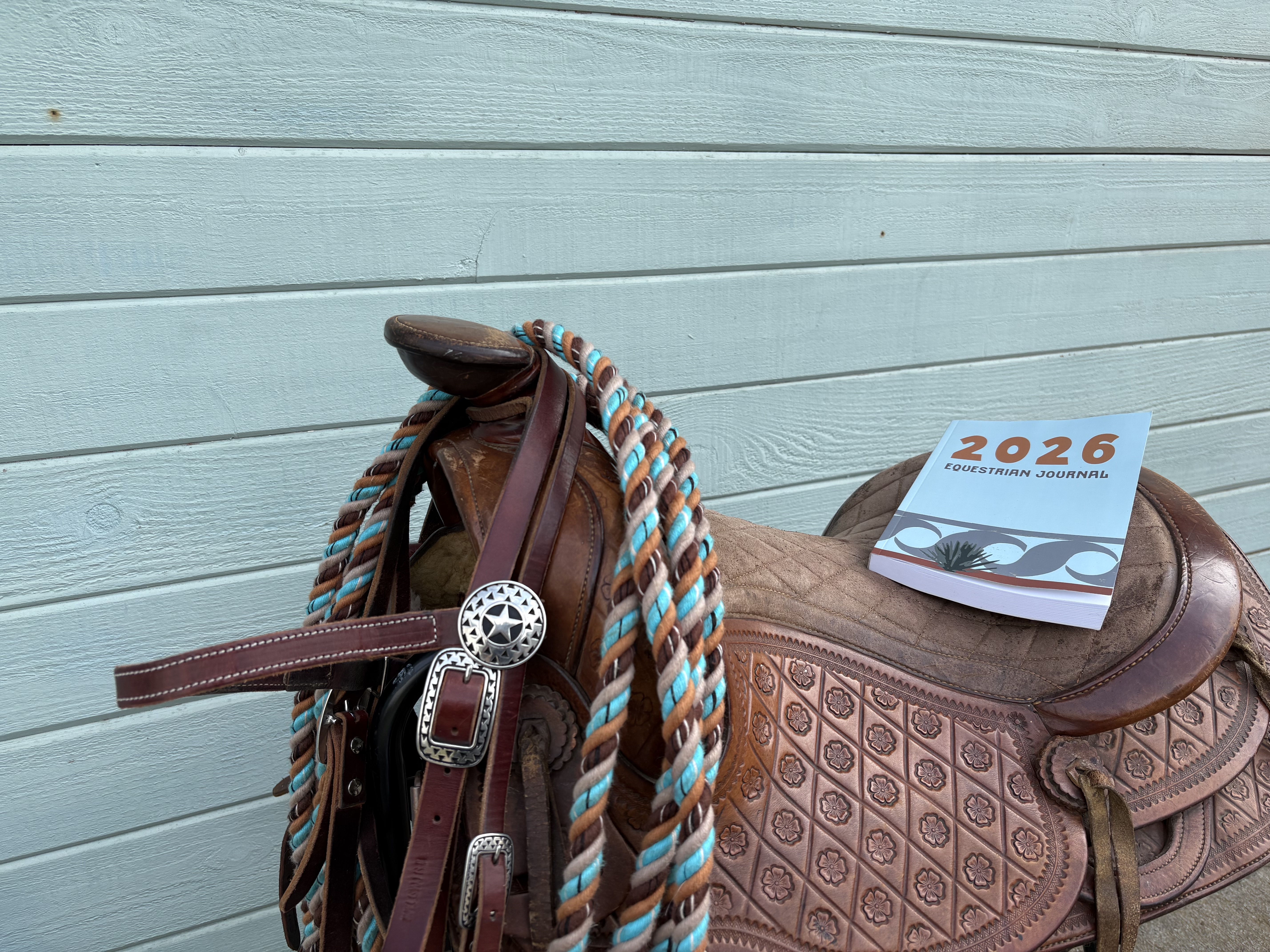 Photo of the 2026 Equestrian Journal sitting on a saddle with western headstall and beautiful cotton mecate reins hanging from saddle horn.